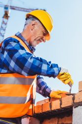 Construction worker in reflective vest and hardhat laying bricks using spatula